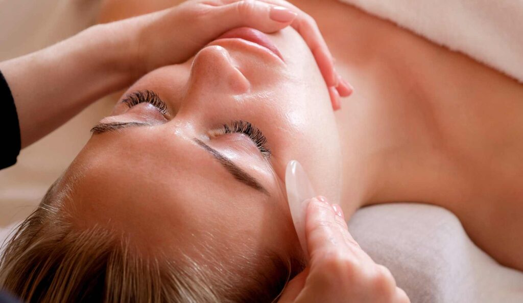 Kvinde får afslappende gua sha massage med en rosakvarts sten under ansigtsbehandling/facial i klinik på Nørrebro