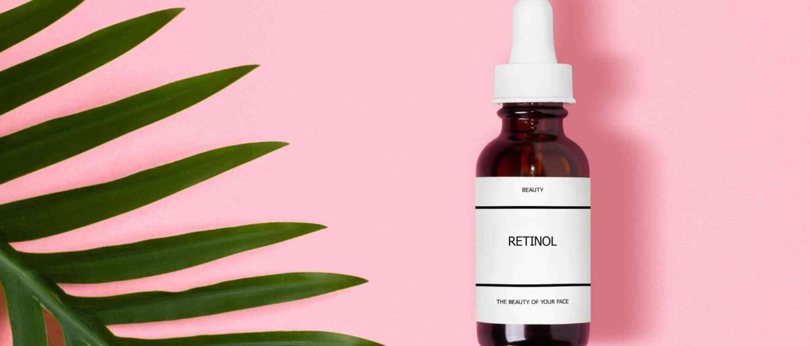 lille flaske retinol på lyseroed baggrunf, med groen palme i venstre hjoerne