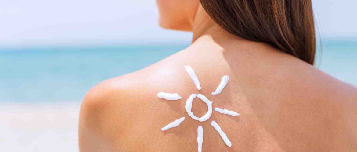 kvinde med afklædt ryg på stranden, har tegnet en sol på ryggen i form af solcreme